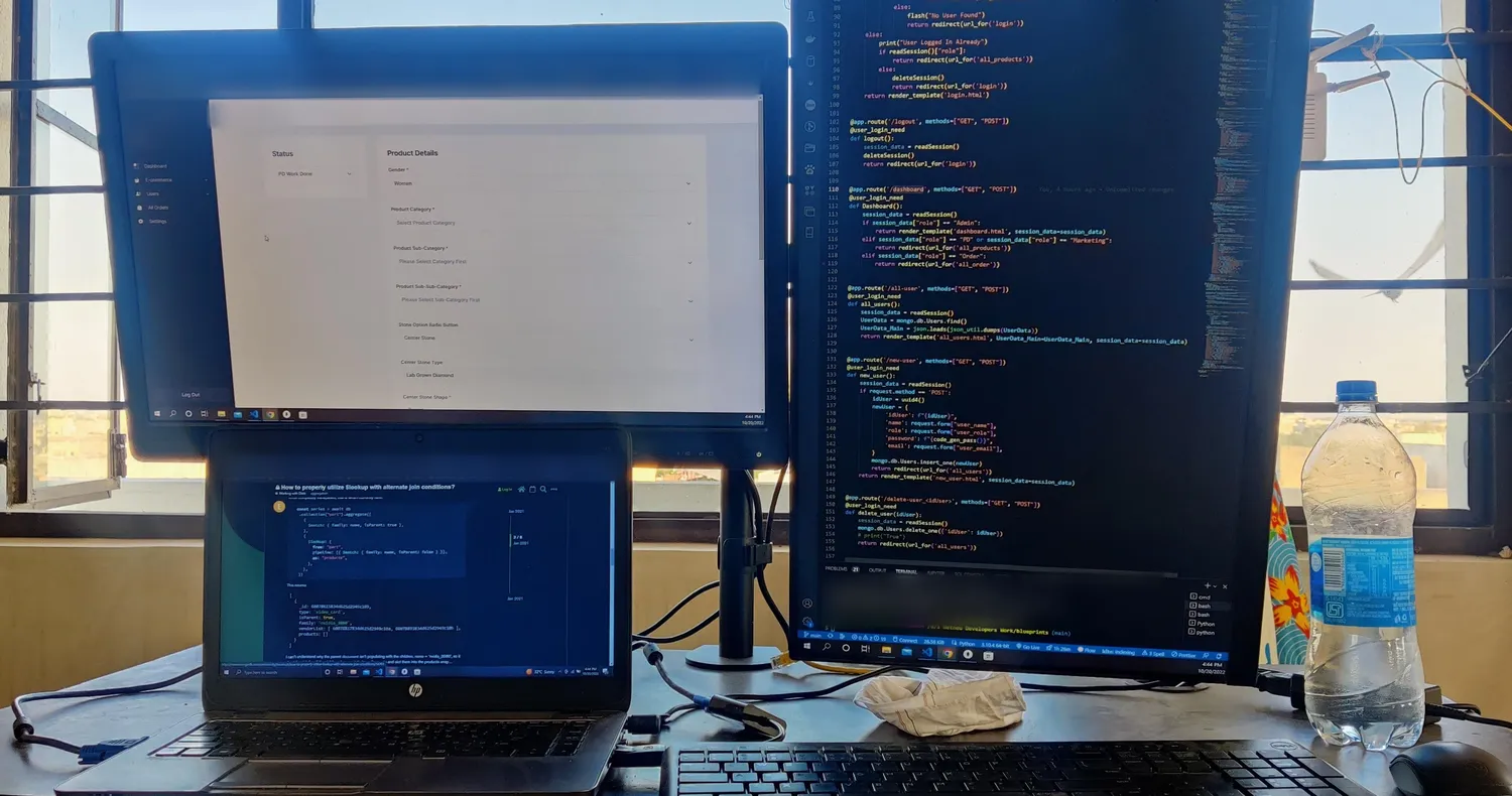 My office in October 2022 by a window: a wide monitor with an ERP I was building for a jewellery client, a vertical monitor full of Python code, and a laptop below them.