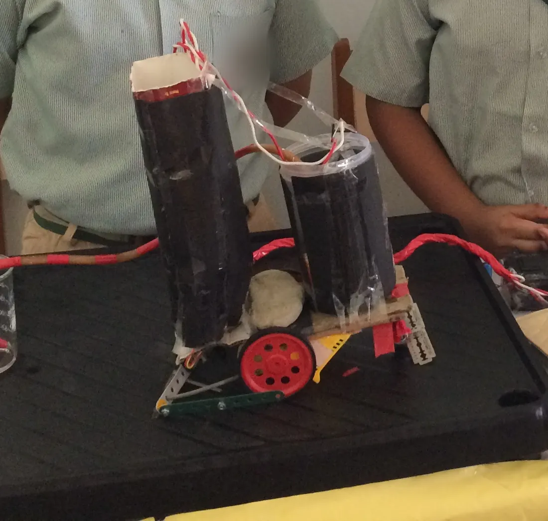 My automatic farming machine on the exhibition table in July 2016: a wheeled base with two tall black tanks, tubes and a beaker for watering.